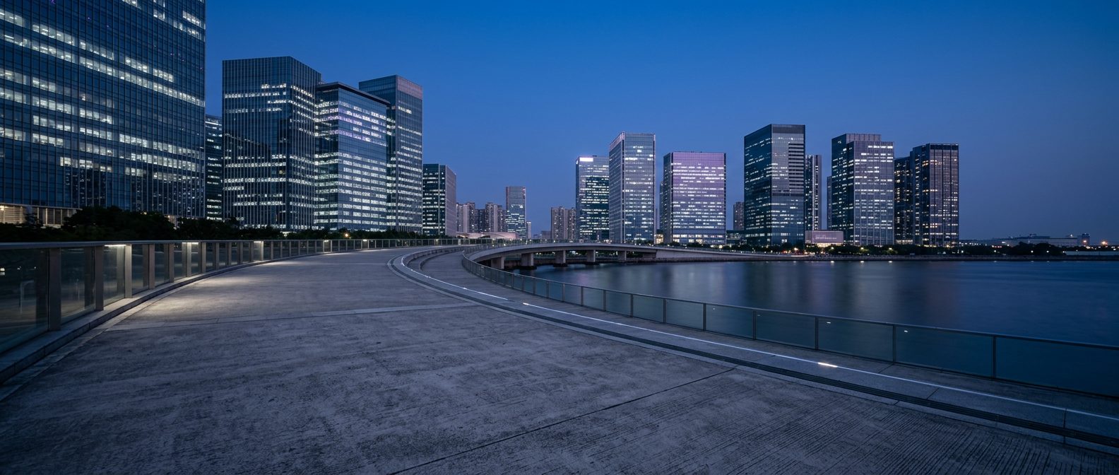 A waterfront walkway beside a financial district at dusk