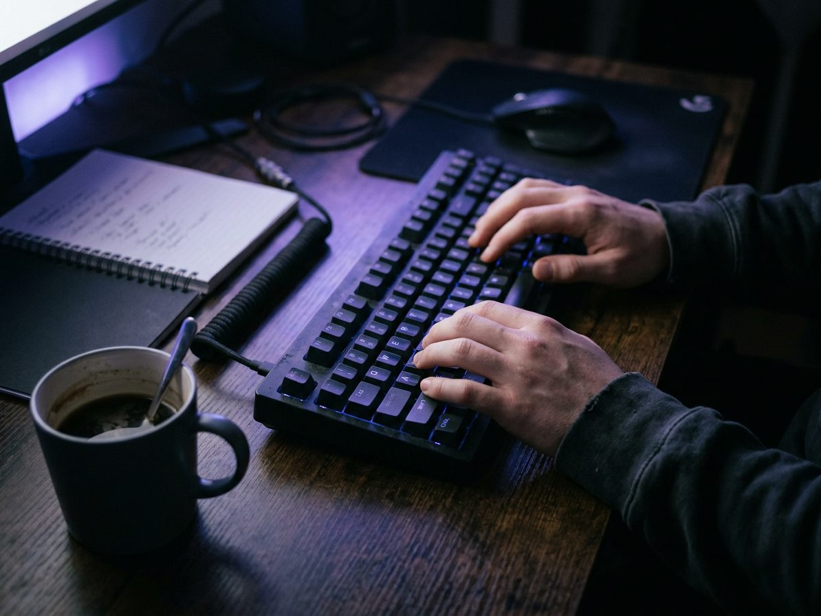 Hands at a keyboard in a dim room lit only by screen glow